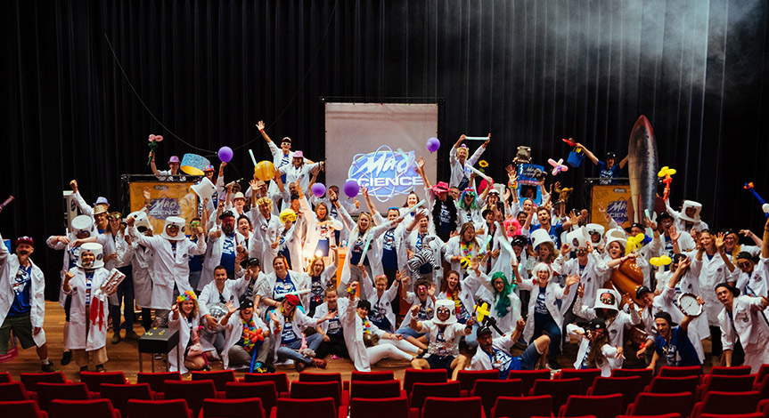 Mad Scientist on stage all wearing mad science lab coats with hands in the air wearing and holding different props