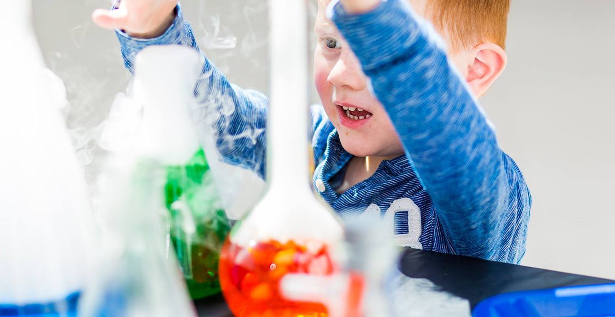 Boy playing with beakers with red and green liquid inside and smoke pouring out